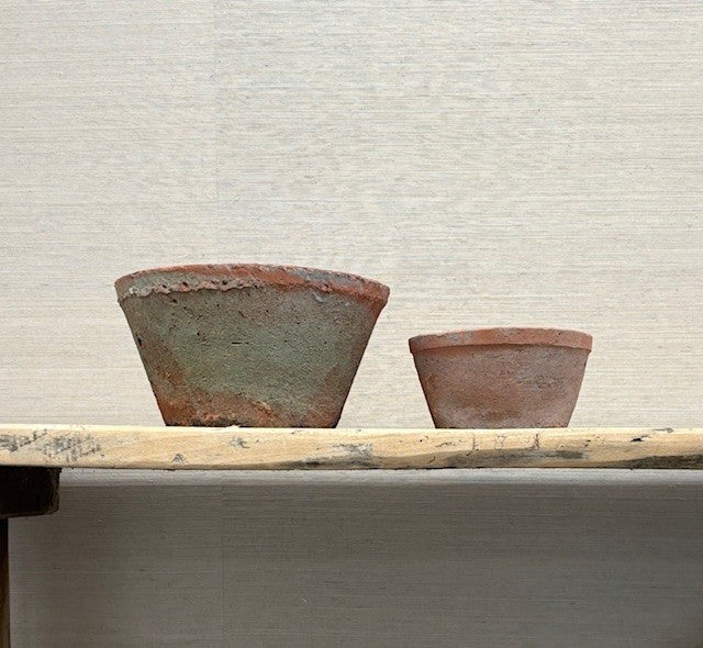 Two terracotta pots on a wooden table against a neutral background