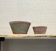 Two terracotta pots on a wooden table against a neutral background