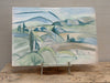 Painting of a landscape with hills and a figure on an easel against a wooden background