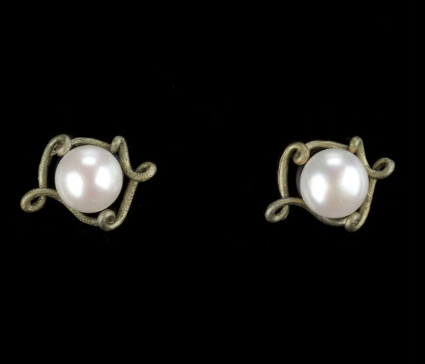 A pair of vintage-style stud earrings featuring round white pearls set in an ornate, textured antique bronze or silver-toned scrollwork frame, presented on a solid black background.