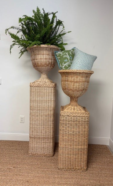 Two wicker plant stands with decorative pillows and a plant against a white wall.