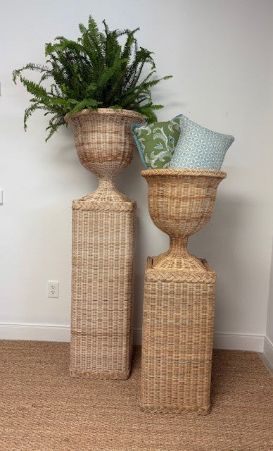 Two wicker plant stands with decorative pillows and a plant against a white wall.