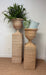 Two wicker plant stands with decorative pillows and a plant against a white wall.