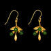 A pair of gold dangle earrings with green bead details, shown against a solid black background.