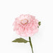 A single artificial pink flower with layered petals, a yellow-tinted center, and green leaves on a stem, photographed against a plain white background.