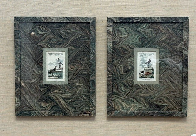 Two framed artworks with feathered patterns on a wooden wall.