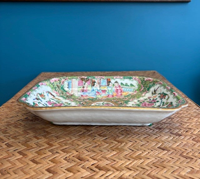 Decorative ceramic platter with a colorful design on a woven surface against a blue wall.