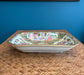 Decorative ceramic platter with a colorful design on a woven surface against a blue wall.