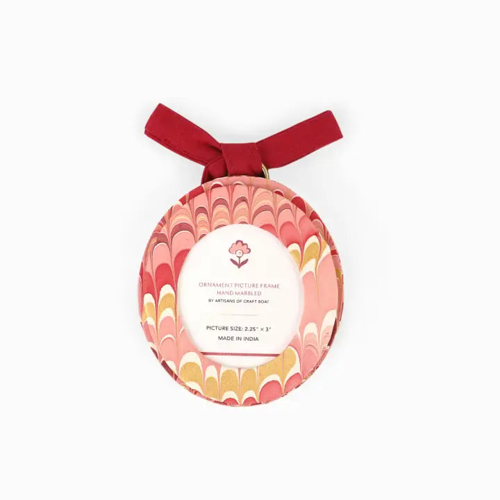 A round hand-marbled ornament picture frame with a red ribbon loop at the top, featuring a pink, red, and gold marbled pattern on a white background.