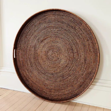 Large round woven basket on a wooden floor against a white wall