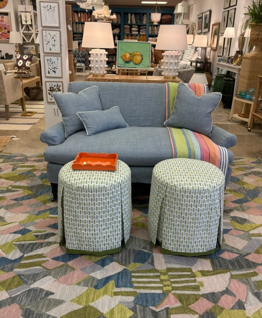 Blue sofa with patterned cushions and stools on a colorful rug in a store setting.