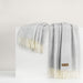 Gray throw blanket with white fringe on a white surface
