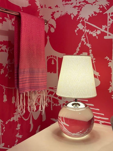Lamp with a white shade and red base on a surface against a red wall with white patterns