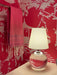 Lamp with a white shade and red base on a surface against a red wall with white patterns