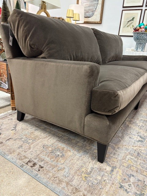 Brown sofa with cushions on a patterned rug in a room setting.