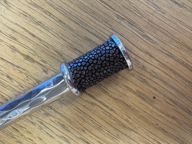 Metallic spreader with black textured grip on a wooden surface