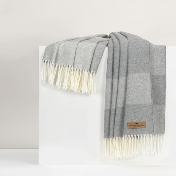 Gray throw with white fringes draped over a white surface