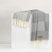 Gray throw with white fringes draped over a white surface