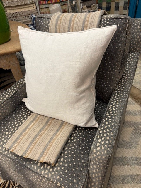 Gray cushioned chair with a white pillow and striped throw