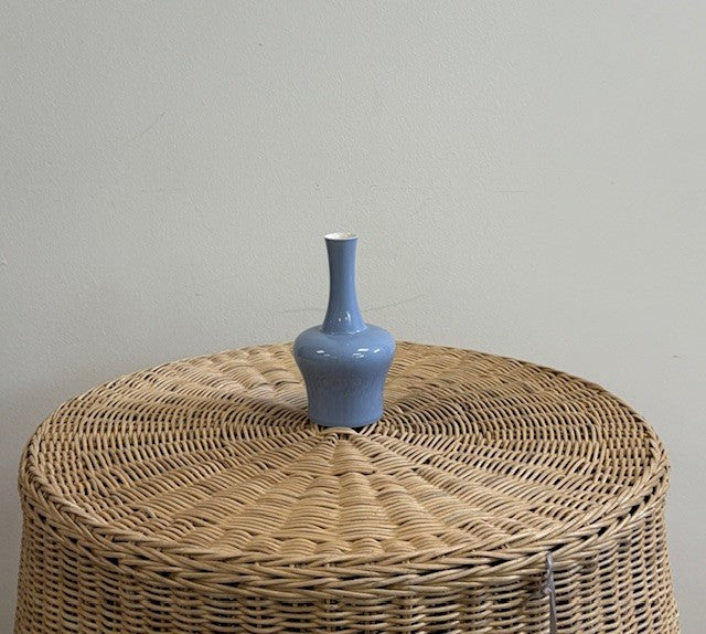 Blue vase on a woven ottoman against a plain wall