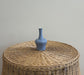 Blue vase on a woven ottoman against a plain wall