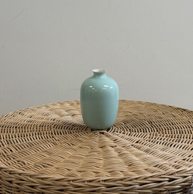 Light blue ceramic vase on a woven surface with a plain background