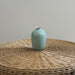Light blue ceramic vase on a woven surface with a plain background