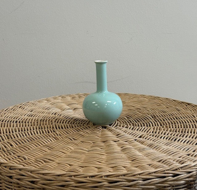 Light blue ceramic vase on a woven surface with a plain background