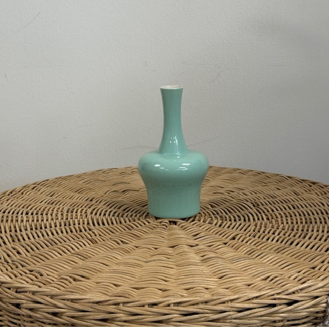 Light blue ceramic vase on a wicker surface with a plain background