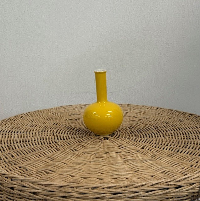 Yellow vase on a wicker surface with a plain background