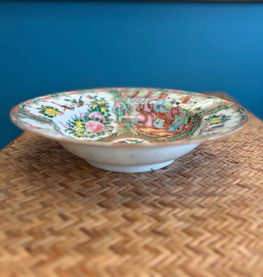 Decorative ceramic bowl with colorful patterns on a woven surface against a blue wall.
