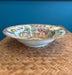 Decorative ceramic bowl with colorful patterns on a woven surface against a blue wall.
