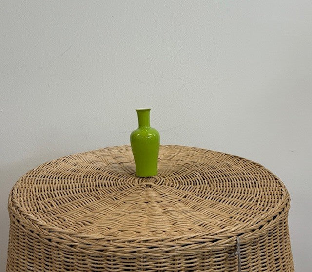 Green vase on a woven stool against a plain background