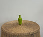 Green vase on a woven stool against a plain background