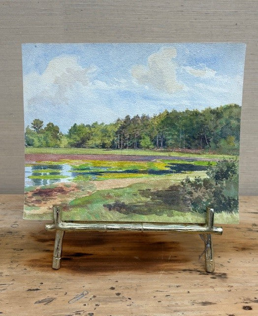 Painting of a landscape with trees and water on an easel.