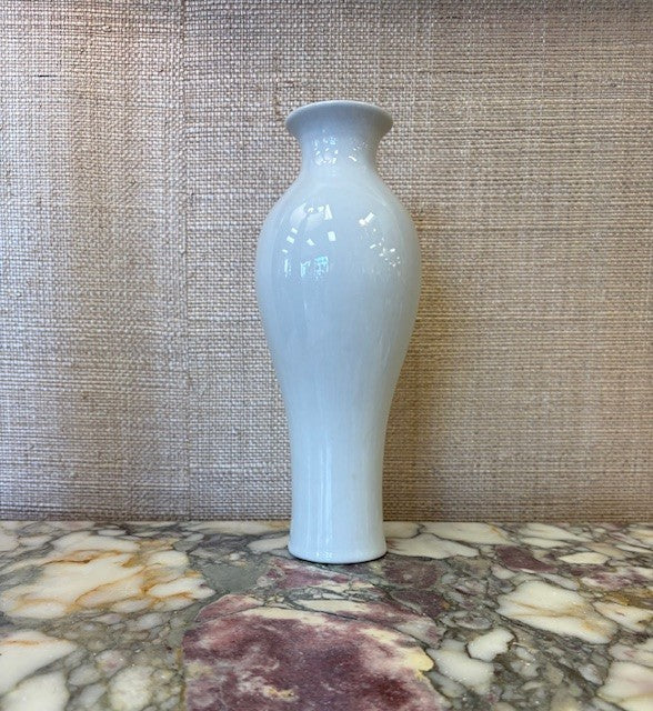 White ceramic vase on a marble surface with a textured wall background