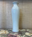 tall White ceramic vase on a textured surface with a neutral background