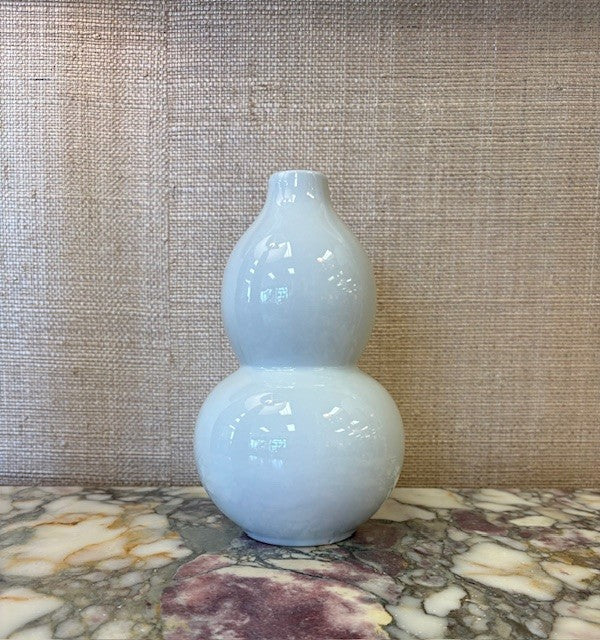 white ceramic double-gourd vase on a marble surface with a textured wall background