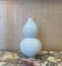 white ceramic double-gourd vase on a marble surface with a textured wall background