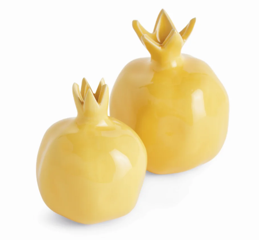 Two glossy yellow pomegranate-shaped decorative objects on a clean white background.