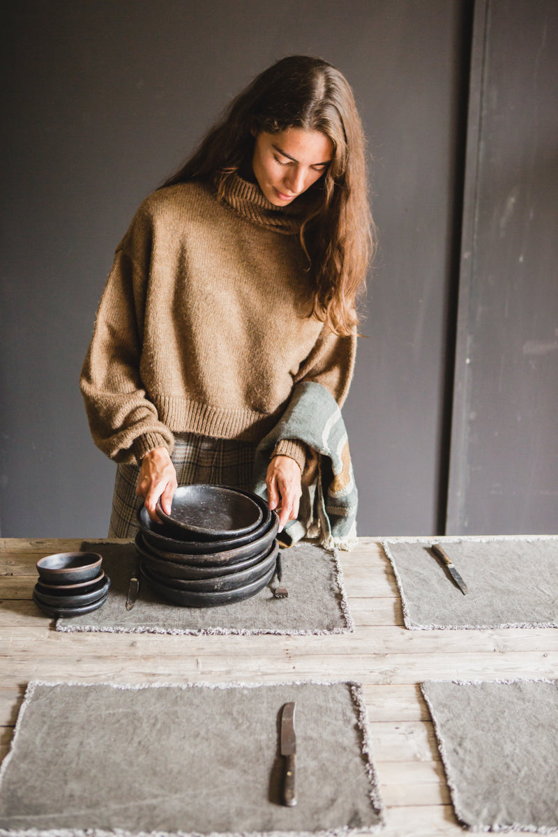 woman setting table with linen placemats and dark pottery
