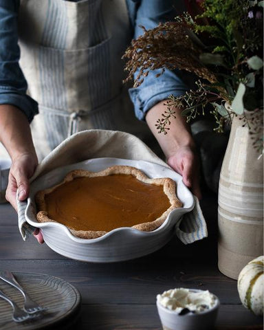 a baker showing a pie in hand-thrown pottery pie dish