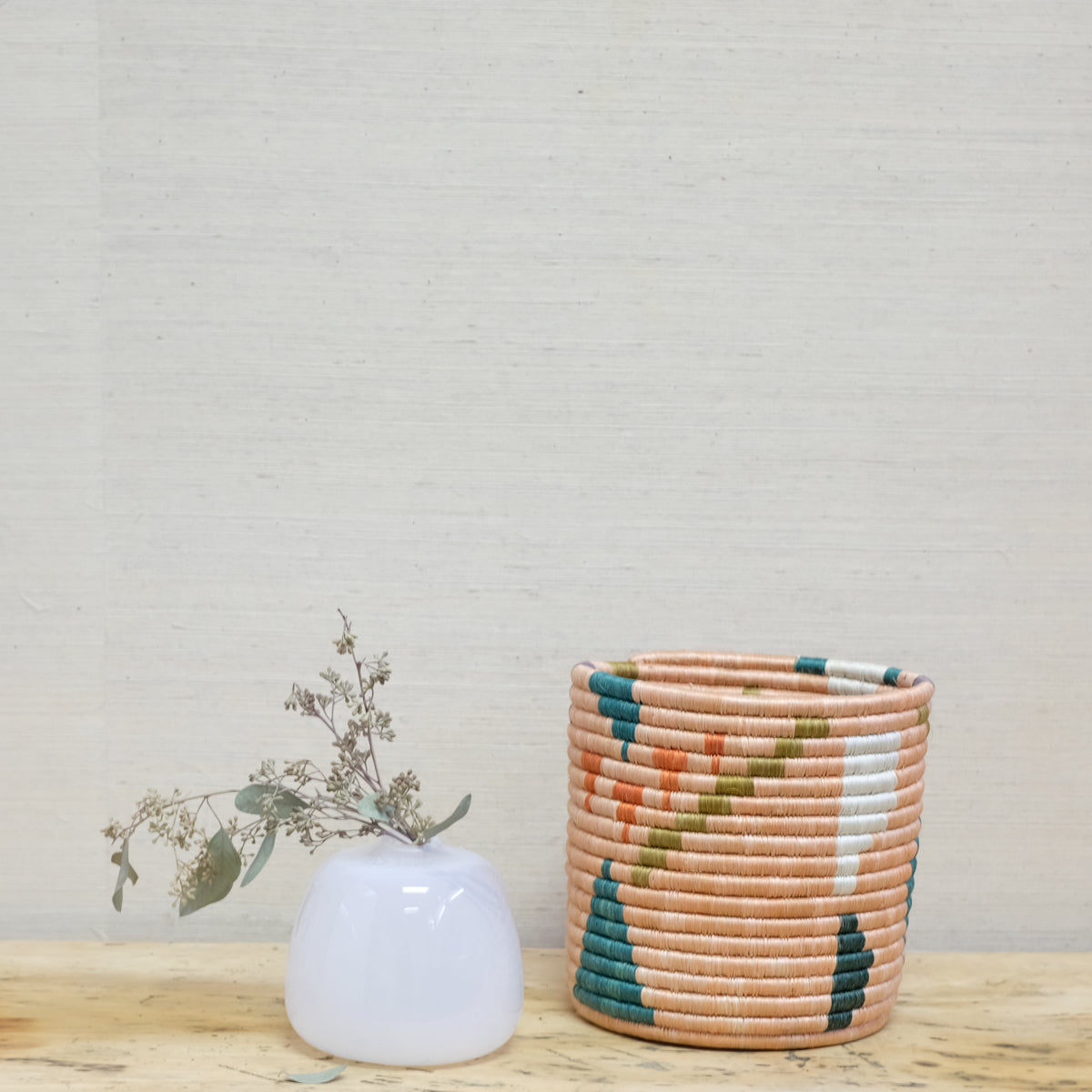 colorful handwoven grass basket next to white glass vase