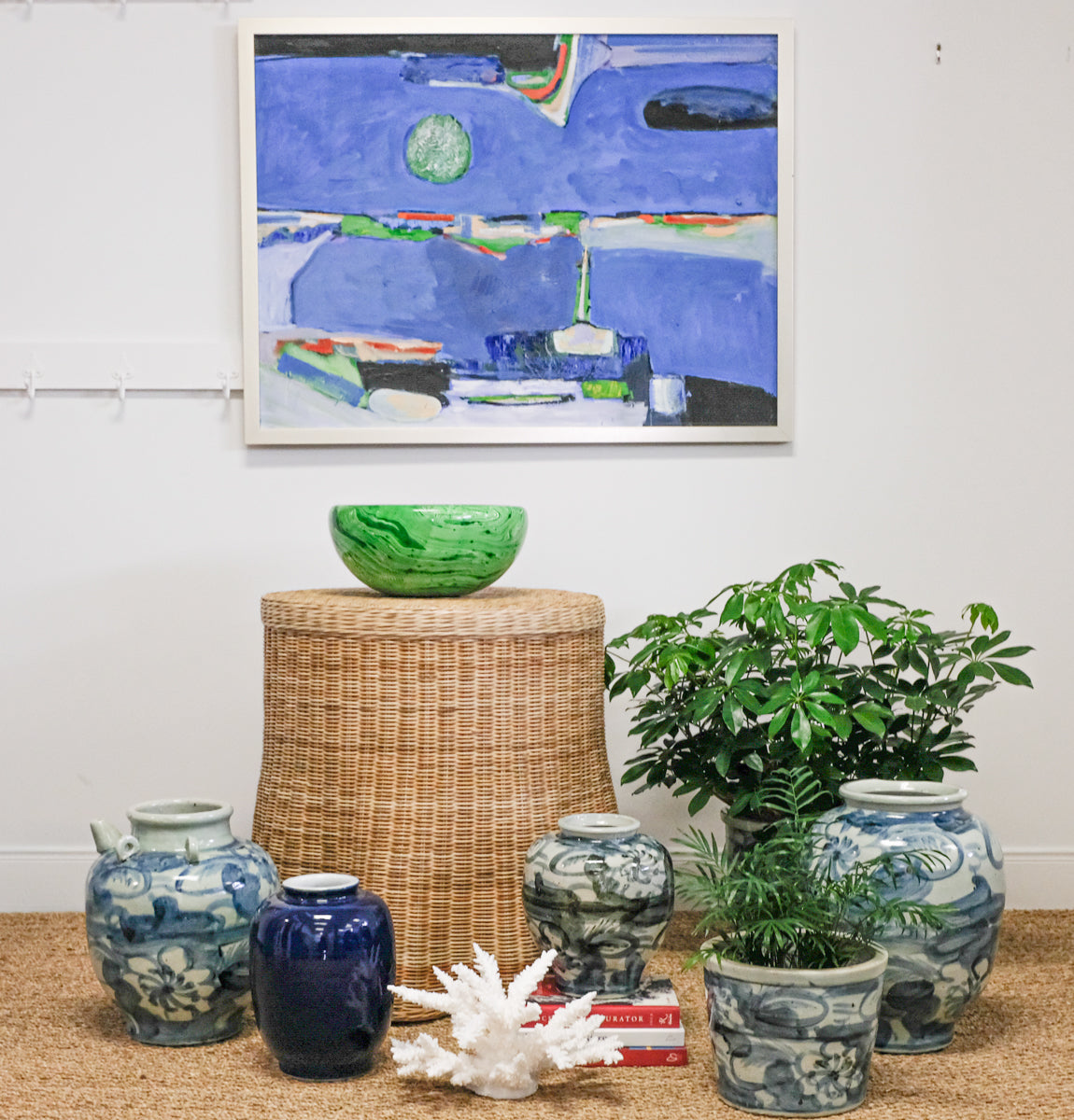 abstract artwork surrounded by blue and white pottery with one green bowl on top of wicker table