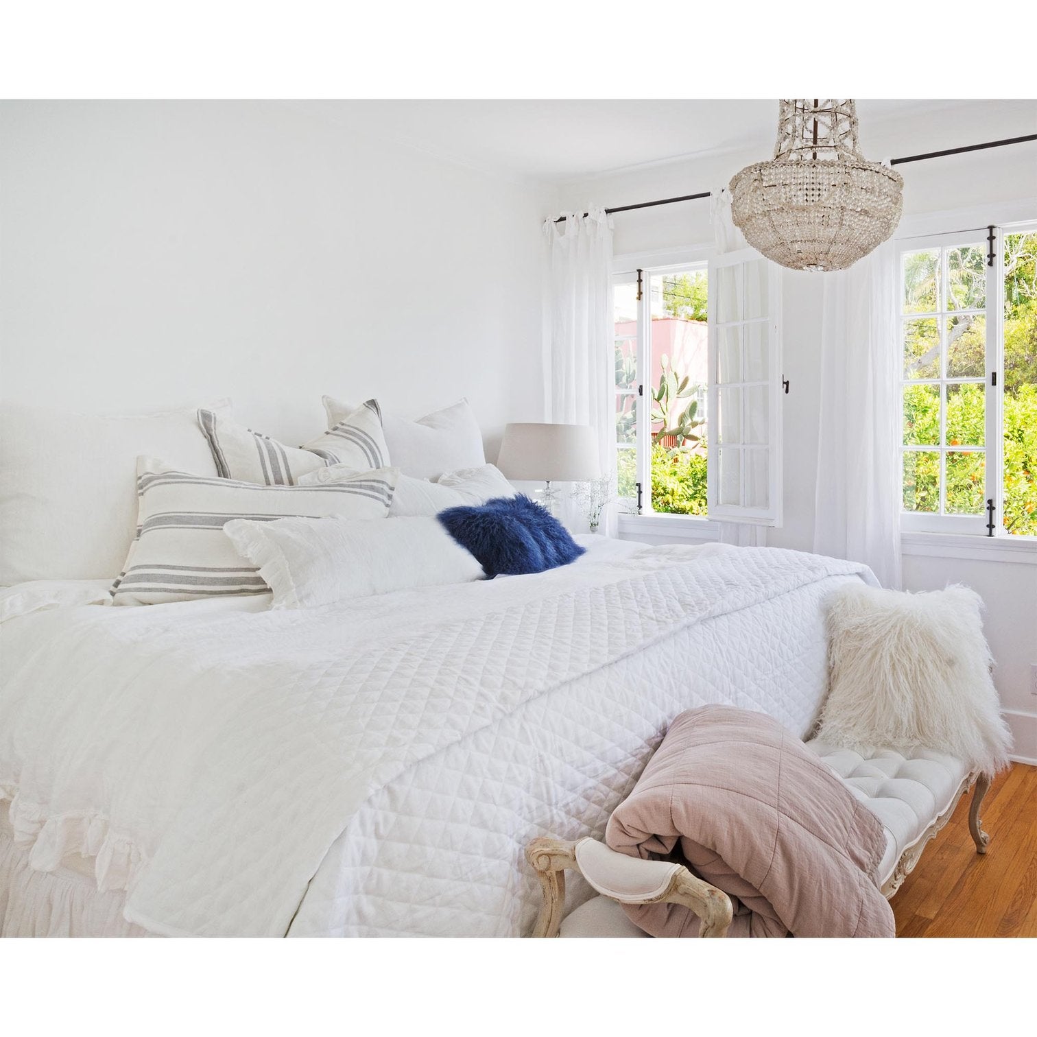 white quilted coverlet on bed with chandelier and velvet bench