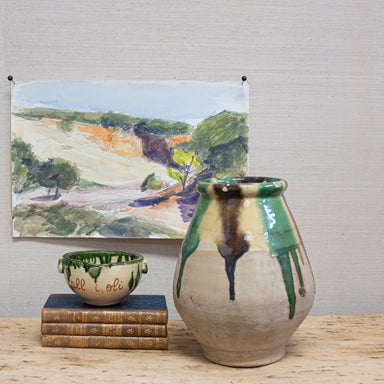 terra cotta pot with dripping glaze in front of watercolor artwork and beside a stack of books
