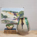 terra cotta pot with dripping glaze in front of watercolor artwork and beside a stack of books